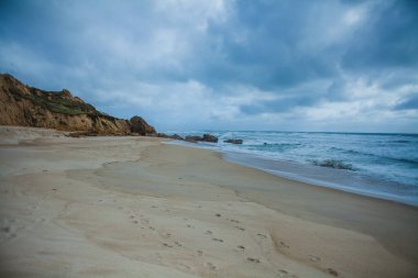 Kıyı manzarası kıyı şeridi boyunca uzanan kumlu bir plaj. Resmin sol tarafında kaya oluşumlarının farklı katmanlarına sahip altın kayalıklar var.