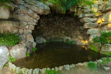 Doğal kaya oluşumları ve yeşil yapraklarla çevrili küçük, sakin bir göleti olan gölgeli bir taş mağara.