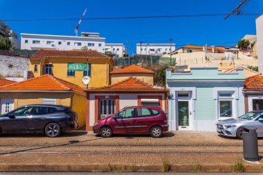 Porto, Portekiz 'de renkli ve geleneksel evlerin yer aldığı canlı bir sokak sahnesi. Evler, biri sarı, diğeri pastel yeşile, üçüncüsü ise kırmızı ve bej karışımı olarak çeşitli tonlarda boyanmıştır..