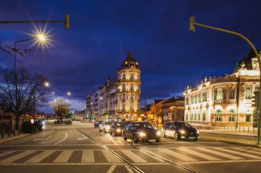 Canlı bir gece şehri. Işıklı tarihi binalar, parlayan sokak lambaları, yıldız patlaması efektleri ve hareketli şehir kavşağından geçen araçlar.