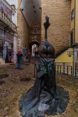 Bir Avrupa şehrinde, bir ortaçağ kapısı ve tarihi binaların önündeki kaldırım taşı meydanında stilize olmuş bir ud oyuncusunun bronz heykeli duruyor.