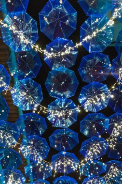 Mavi şemsiyeler ve beyaz ışıklarla süslenmiş bir cadde gece neşeli ve büyülü bir atmosfer yaratır.