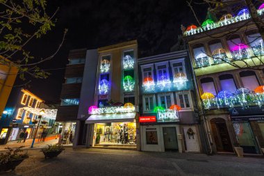 Bir cadde boyunca binalar şenlikli bir gece sahnesi için renkli şemsiyeler ve ip ışıklarıyla süslenir.