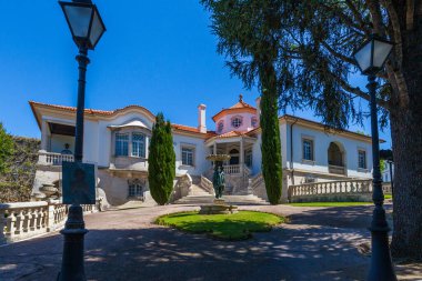 Beyaz cepheli, kırmızı kiremitli, etrafı manikürlü bahçe ve zarif elektrik direkleriyle çevrili büyük bir malikane.