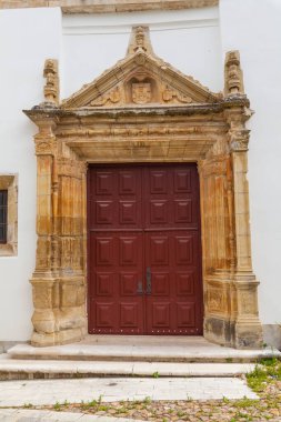 Süslü bir kapı, oyulmuş taş bir çerçeve ve tarihi bir binaya açılan büyük ahşap bir kapı.
