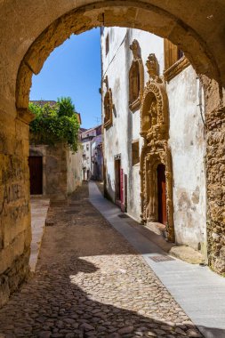 Taş kemerli dar, kaldırım taşı bir cadde. Süslü taş işçiliği olan tarihi bir binaya açılıyor.