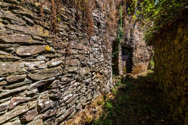 İki taş duvar arasındaki dar, fazla gelişmiş bir geçit. Gizemli ve terk edilmiş bir binaya açılıyor.
