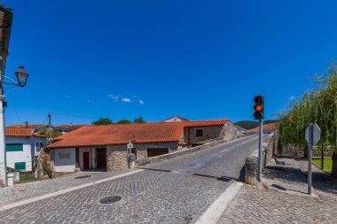 Kırmızı kiremit çatılı tarihi bir taş köprü, Portekiz 'in pitoresk bir köyünde küçük bir nehir veya akarsu boyunca uzanır.