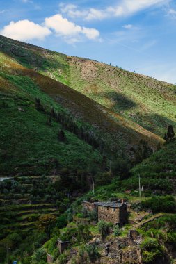 Bereketli yeşil bitki örtüsüyle kaplı huzurlu, manzaralı bir yamaç ve dağınık bulutlu mavi gökyüzünün altındaki teraslarda yuva yapmış büyüleyici bir taş kulübe.