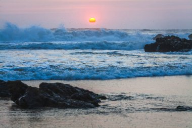 Güneş ufka doğru batarken, sıcak turuncu ve pembe bir tonu gökyüzüne yayar ve suya yansıtır.