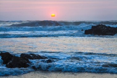 Güneş ufka doğru batarken, sıcak turuncu ve pembe bir tonu gökyüzüne yayar ve suya yansıtır.