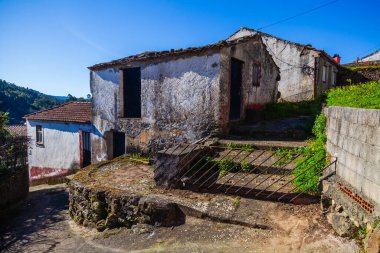 Yeşillik ve kırsal cazibeyle çevrili sakin bir caddede seramik çatılı, yıpranmış, beyaz bir ev duruyor.