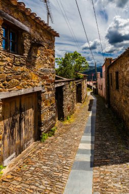 Dar bir kaldırım taşı ara sokağı taş duvarlarla çevrili tuhaf bir köyden geçiyor ve bulutlu bir gökyüzünün altındaki mesafeye doğru yol alıyor.