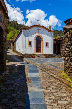 Büyüleyici bir köyde haçı olan, neşeli ışıklarla süslenmiş ve taş binalarla çevrili tuhaf beyaz bir şapel.