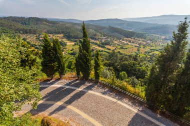Ağaçlarla çevrili dolambaçlı bir taş patika yuvarlanan tepeler, tarım arazileri ve Portekiz 'in uzak dağlarının panoramik bir görüntüsünü sunar.