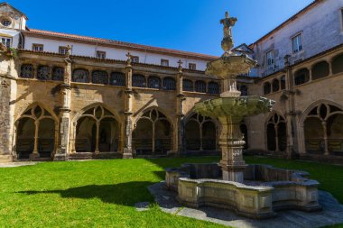 Gotik kemerler ve parlak kiremitlerle çevrili merkezi taştan bir çeşme ile pitoresk bir manastır avlusu, açık mavi gökyüzü altında, tarihi mimarinin bir zemin üzerine kurulmuş.
