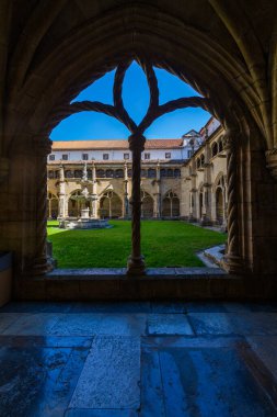 Merkezi bir çeşmesi ve yemyeşil çimenliği olan geleneksel bir manastır avlusunun fevkalade manzarası. Kemerli bir pencereyle çerçevelenmiş, berrak mavi bir gökyüzü sunuyor.
