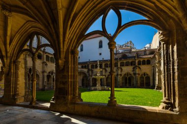 Güneşli bir Gotik manastır manzarası, uzun atari salonları, çeşmeli merkezi yeşil bir avlu ve berrak mavi gökyüzünün altında parlak beyaz bir mimari bina