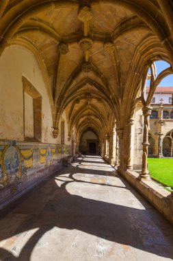 Sunlit Gotik manastırı, uzun atari salonları, fıskiyeli merkezi yeşil bir avlu ve berrak mavi gökyüzünün altında parlak beyaz bir mimari bina.