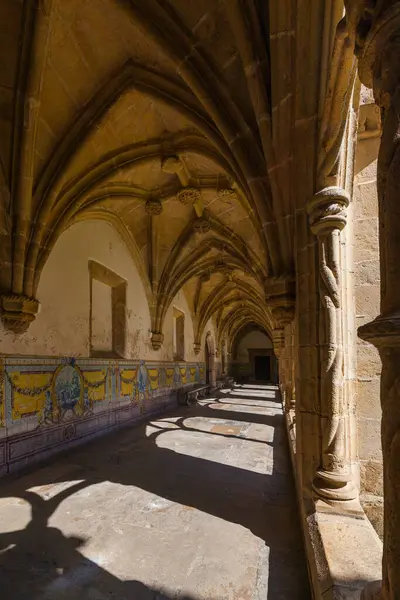 Sunlit Gotik manastırı, uzun atari salonları, fıskiyeli merkezi yeşil bir avlu ve berrak mavi gökyüzünün altında parlak beyaz bir mimari bina.