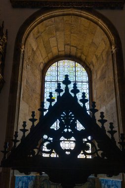 Geometrik kurşunlu cam desenli tarihi bir kemerli pencerenin çarpıcı bir görüntüsü, parlak dış aydınlığa karşı süslü ahşap bir kilise mobilyasını siluetliyor.