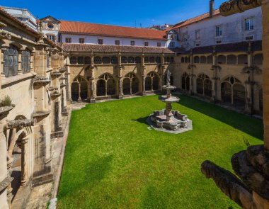 Gotik kemerler ve parlak kiremitlerle çevrili merkezi taştan bir çeşme ile pitoresk bir manastır avlusu, açık mavi gökyüzü altında, tarihi mimarinin bir zemin üzerine kurulmuş.