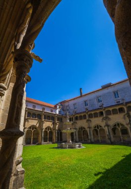 Gotik kemerler ve parlak kiremitlerle çevrili merkezi taştan bir çeşme ile pitoresk bir manastır avlusu, açık mavi gökyüzü altında, tarihi mimarinin bir zemin üzerine kurulmuş.