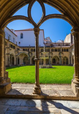 Merkezi bir çeşmesi ve yemyeşil çimenliği olan geleneksel bir manastır avlusunun fevkalade manzarası. Kemerli bir pencereyle çerçevelenmiş, berrak mavi bir gökyüzü sunuyor.