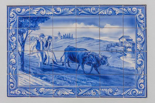 Mavi-beyaz seramik seramik duvar resmi, iki çiftçinin sakin bir kırsal alana karşı bir öküzle tarlayı sürüşünü gösteriyor.