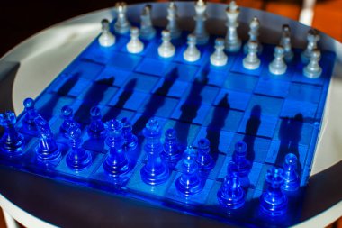 Yarı saydam mavi parçalar ve karelerle büyüleyici bir satranç tahtası, karmaşık gölgeler, görsel ve stratejik bir sahne yaratır.