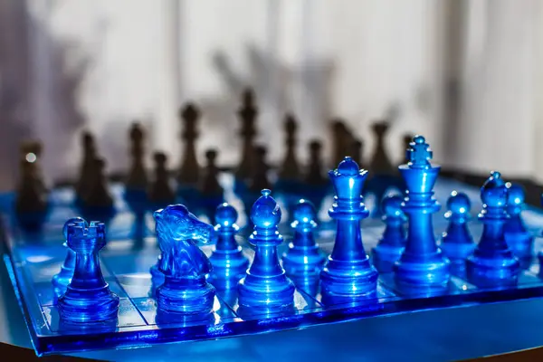 Canlı bir satranç tahtası keskin odak noktasında, arka planda bulanık ahşap parçalarla çelişen yarı saydam mavi parçalar içerir, dinamik ve görsel olarak çarpıcı bir kompozisyon oluşturur.