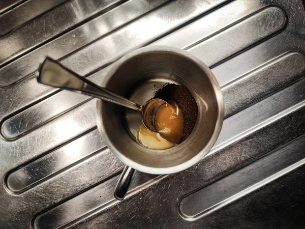 咖啡粉和一汤匙蜂蜜放在金属底座上的金属杯子里 免版税图库图片
