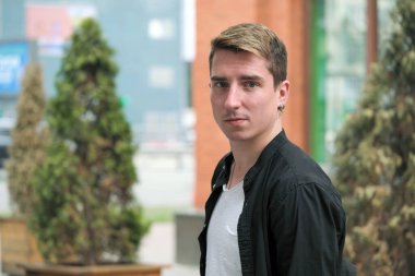 Portrait of a young handsome guy in a black shirt close-up autumn street photography