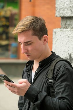 Siyah tişörtlü, akıllı telefon ekranlı sokak fotoğrafçılığına bakan yakışıklı bir adamın portresi.