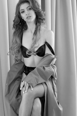 Uzun dalgalı saçlı, yağmurluk ve file çorapla poz veren güzel kahverengi saçlı kadın.