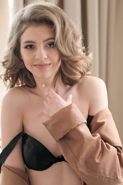 stock image Portrait of a young beautiful attractive glamorous brown-haired woman with wavy hair in a brown raincoat on black lingerie in the studio