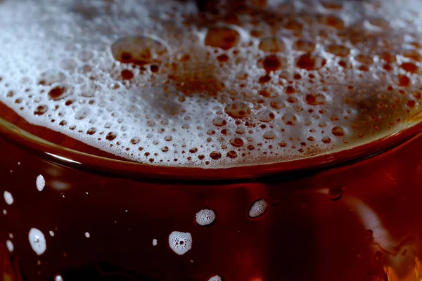 Fresh cold light barley beer is poured into a glass glass on a black background close-up