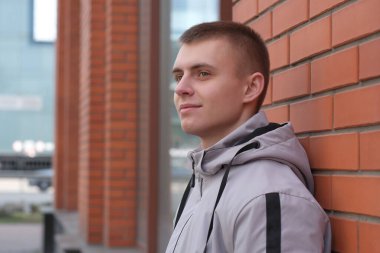 Bahar şehrinin caddesinde, kırmızı tuğla duvarın yanında kısa saçlı yakışıklı bir adamın portresi.