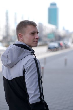 Güneşli bir günde, bir bahar şehrinin sokağında kısa saçlı yakışıklı bir gencin portresi.