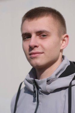 Güneşli bir günde, bir bahar şehrinin sokağında kısa saçlı yakışıklı bir gencin portresi.