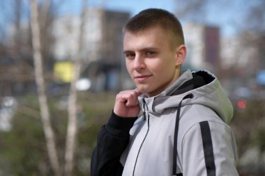 Güneşli bir günde, bir bahar şehrinin sokağında kısa saçlı yakışıklı bir gencin portresi.