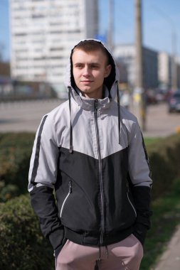 Güneşli bir günde, bir bahar şehrinin sokağında kısa saçlı yakışıklı bir gencin portresi.