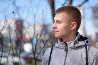 Güneşli bir günde, bir bahar şehrinin sokağında kısa saçlı yakışıklı bir gencin portresi.