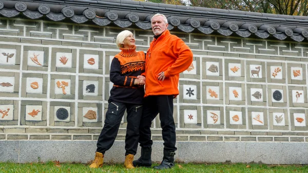 オレンジ色のセーターを着た秋の日本庭園の壁を背景に 高齢者の白髪楽観的なカップルの男性と女性 — ストック写真