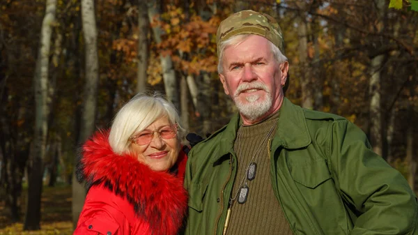 高齢者の白髪のカップルの肖像 軍事化されたカーキの服の男 オレンジのジャケットの女性 街の秋 — ストック写真