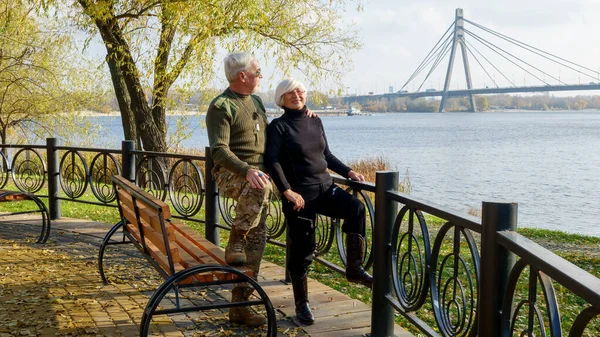 stock image Portrait of an elderly gray-haired couple, a man in militarized khaki clothes, a woman in a black sweater, in autumn in the city on the embankment of the river