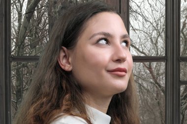 Pencerenin arka planında beyaz kazaklı güzel bir genç kadının portresi.