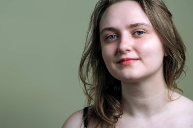 Portrait of a young attractive brown-haired girl in a black dress on a green background close-up