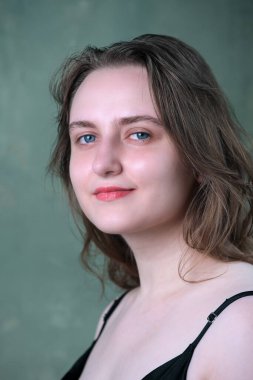 Portrait of a young attractive brown-haired girl in a black dress on a green background close-up
