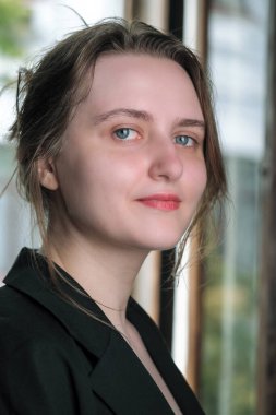 Siyah ceketli çekici kahverengi saçlı bir kızın portresi açık bir pencerenin önünde.